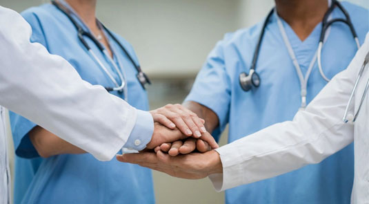 Two doctors holding hands with one doctor wearing a stethoscope.