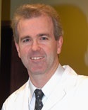 A man in white coat and tie smiling for the camera.